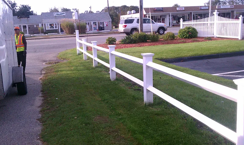 Mowed and edged lawn along a white vinyl fence at a commercial plaza in Massachusetts
