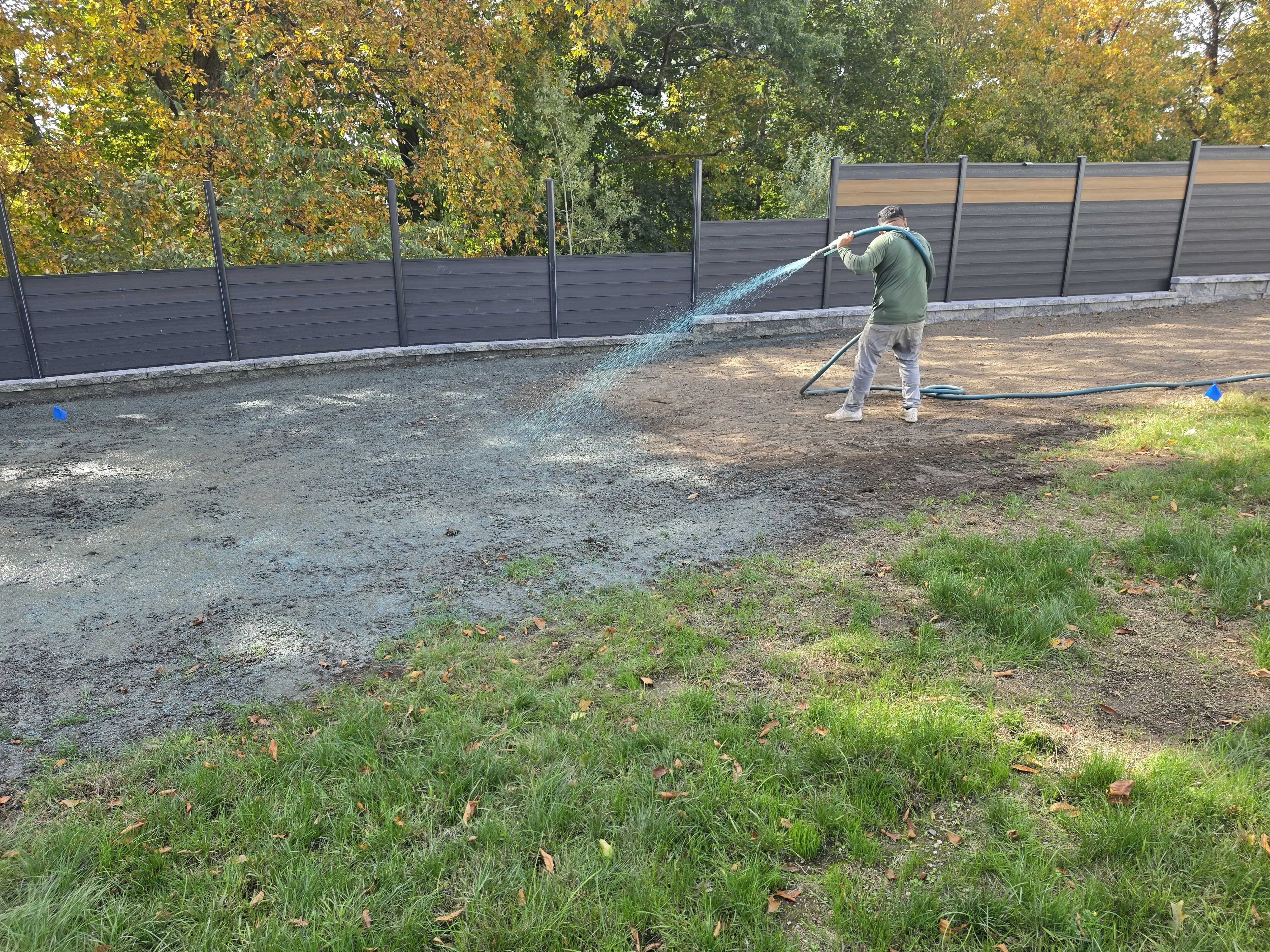 Crew member spraying hydroseed over a graded yard along a new fence in Massachusetts